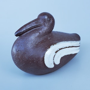 May include: A brown ceramic bird sculpture with white accents. The bird has a long beak and a rounded body. The sculpture is a unique and decorative piece.