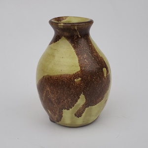 May include: A small, light green ceramic vase with brown splotches and a rounded body.