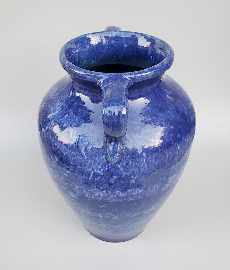Op de afbeelding: Een grote blauwe keramische vaas met twee handvatten. De vaas heeft een gevlekt blauw glazuur met een wit marmereffect.