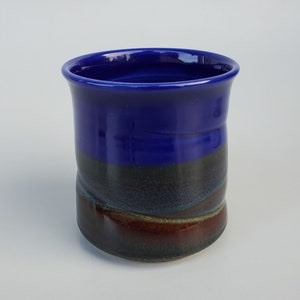 May include: A blue and brown ceramic mug with a glazed finish. The mug has a wide, rounded base and a slightly flared lip.