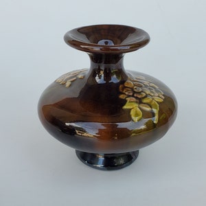 May include: A brown ceramic vase with a wide base and a narrow neck. The vase is decorated with a floral design in shades of green, yellow, and brown.