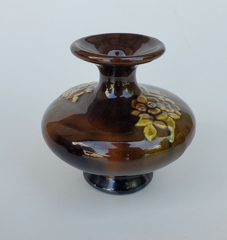 May include: A brown ceramic vase with a wide base and a narrow neck. The vase is decorated with a floral design in shades of green, yellow, and brown.