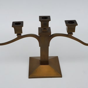 May include: A five-arm brass candelabra with a square base and curved arms. Each arm has a square candle holder.