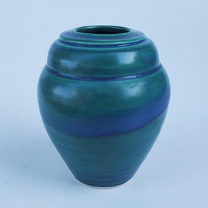 May include: A teal and blue ceramic vase with a rounded body and a narrow opening. The vase features a dark blue band that wraps around the middle. The vase is approximately 8 inches tall.