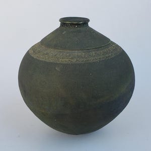May include: A dark green, spherical ceramic vase with a narrow neck and a decorative band around the middle. The vase has a textured surface and a slightly weathered appearance, suggesting an aged or antique aesthetic.