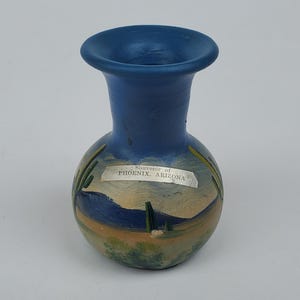May include: A small blue ceramic vase with a painted desert scene and the words "Souvenir of PHOENIX, ARIZONA" on a label.