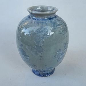 May include: A ceramic vase with a round body and a flared rim. The vase is primarily a muted gray-green color, with blue accents around the rim and base. The surface features a crystalline pattern.