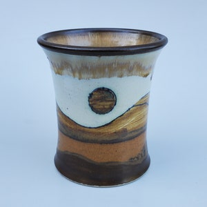 May include: A ceramic vase with a brown, white, and orange abstract design. The vase has a wide mouth and a narrow base.