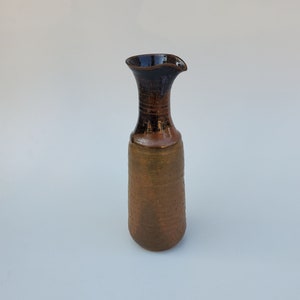 May include: A brown and black ceramic vase with a wide mouth and a textured surface.
