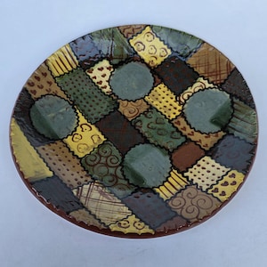 May include: A ceramic tile with a blue and white design featuring an apple, birds, a cat, a dog, a flag, and the letters A, B, C, D, E, and F.