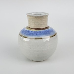 May include: A white ceramic vase with a blue and brown glaze. The vase has a rounded body and a short, cylindrical neck.