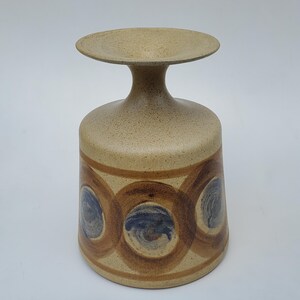 May include: A ceramic vase with a wide, flared base and a narrow neck. The vase is decorated with brown and blue circles.
