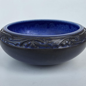 May include: A ceramic bowl with a dark blue exterior and a vibrant blue interior. The rim features a detailed, raised floral pattern. This decorative bowl is suitable for various uses.