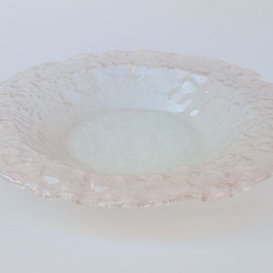 May include: A clear, shallow bowl with a textured, ruffled rim. The bowl has a light pink hue and a smooth, pale centre. The rim has a rough, uneven texture, adding visual interest. The bowl is likely made of glass.
