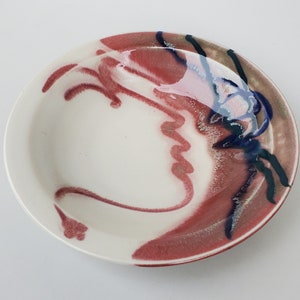 May include: A white ceramic bowl with a red, blue, and green abstract design. The bowl is glazed and has a glossy finish.