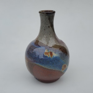 May include: A small, round ceramic vase with a narrow neck. The vase has a speckled white glaze with brown and blue accents.