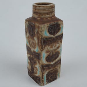 May include: A brown and white ceramic vase with a geometric pattern. The vase has a square base and a narrow neck.