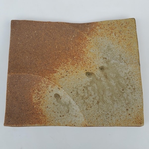 May include: A square ceramic plate with a brown and tan glaze. The glaze has a mottled effect, with areas of darker brown and lighter tan. The plate is slightly irregular in shape, with a slightly raised edge.