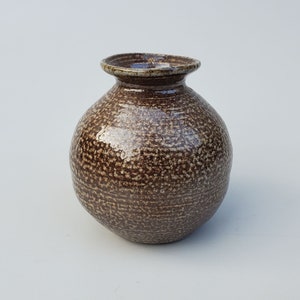 May include: A small, round, brown ceramic vase with a speckled glaze. The vase has a wide mouth and a narrow neck.