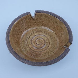May include: A brown ceramic ashtray with a dark brown rim and a spiral design in the center.