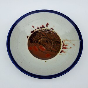 May include: A white ceramic plate with a blue rim and a brown and red design in the center.