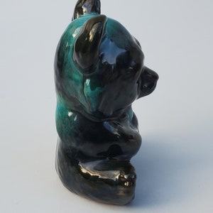 May include: A ceramic bear figurine with a black and green glaze. The bear is sitting with its paws tucked in front of it.