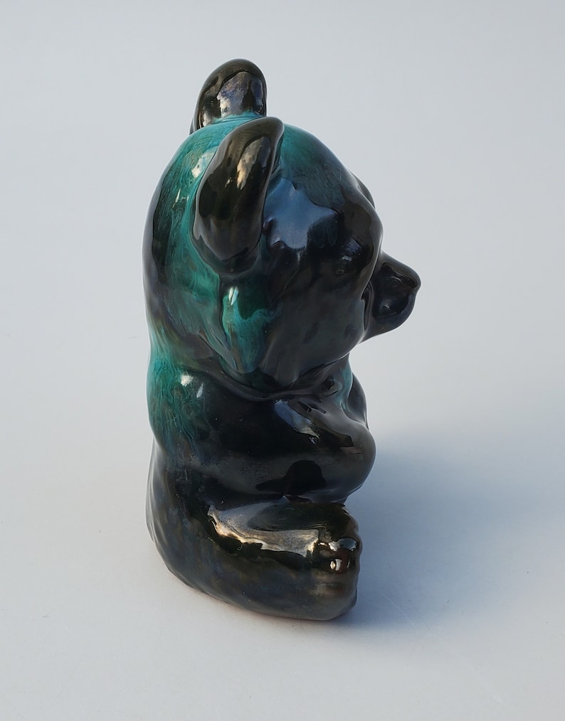 May include: A ceramic bear figurine with a black and green glaze. The bear is sitting with its paws tucked in front of it.