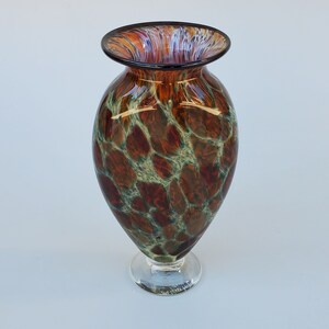 May include: A brown and green glass vase with a mottled pattern. The vase has a wide mouth and a round base. It is signed "Whim Falls" on the bottom.