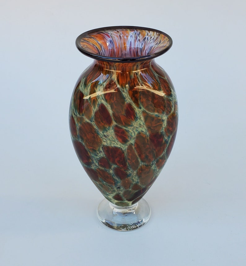 May include: A brown and green glass vase with a mottled pattern. The vase has a wide mouth and a round base. It is signed "Whim Falls" on the bottom.