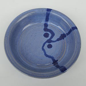 May include: A light blue ceramic bowl with a dark blue glaze design. The bowl has a slightly raised rim and a speckled glaze.