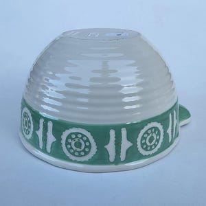 Peut inclure: Un bol en c&eacute;ramique blanc avec une bande vert clair orn&eacute;e d'un motif r&eacute;p&eacute;titif de cercles et de lignes. Le bol a une texture c&ocirc;tel&eacute;e et une petite poign&eacute;e. Le design est simple et &eacute;l&eacute;gant.