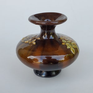 May include: A brown ceramic vase with a wide base and a narrow neck. The vase is decorated with green and white floral designs.