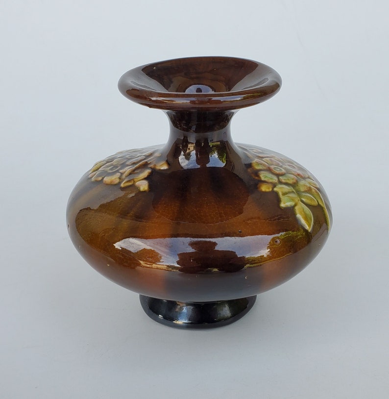 May include: A brown ceramic vase with a wide base and a narrow neck. The vase is decorated with green and white floral designs.