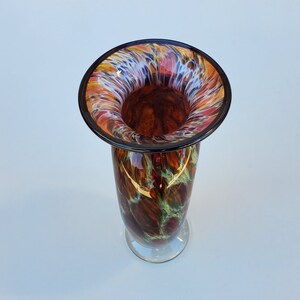 May include: A tall, brown glass vase with a wide, flared opening. The vase has a swirling pattern of white, orange, and red colours. The opening of the vase has a black rim.