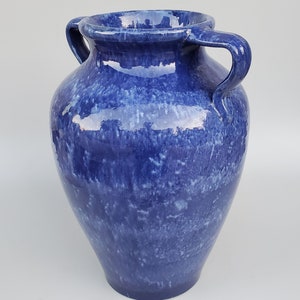 Op de afbeelding: Een blauwe keramische vaas met twee handvatten. De vaas heeft een gevlekt blauwe glazuur met witte stippen.