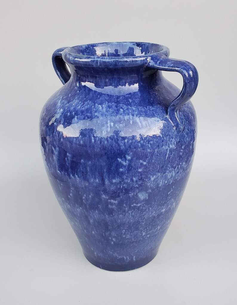 Op de afbeelding: Een blauwe keramische vaas met twee handvatten. De vaas heeft een gevlekt blauwe glazuur met witte stippen.