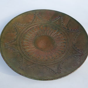 May include: A large, round, ceramic plate with a green and brown glaze. The plate has a raised, geometric design in the center.