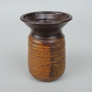 May include: A brown and orange ceramic vase with a wide, flared opening. The vase has a textured, striated surface.