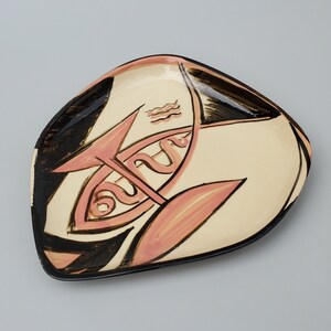 May include: A ceramic serving dish with a unique design featuring a stylized fish with a wavy line and a black and white background. The fish is painted in shades of pink and white.