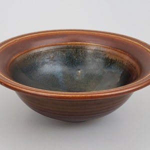 May include: A brown ceramic bowl with a dark blue glaze inside and a brown rim with a thin gold line. The bowl has a slightly flared lip and a rounded bottom.