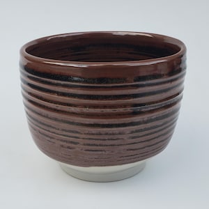 May include: A brown ceramic bowl with a white base. The bowl has a striped pattern in a darker brown color.
