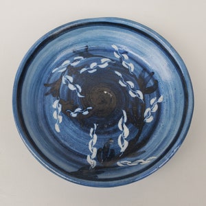 May include: A blue ceramic plate with a white and black floral design. The plate has a slightly raised rim and a smooth, glazed surface.