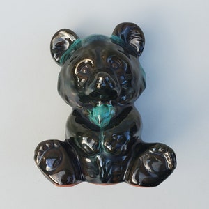 May include: A black ceramic bear figurine with green and blue glaze. The bear is sitting with its paws tucked in front of it.