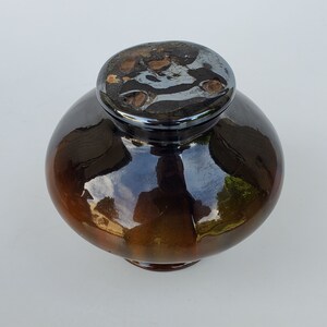 May include: A brown and black ceramic jar with a shiny glaze. The lid is black with a silver design.