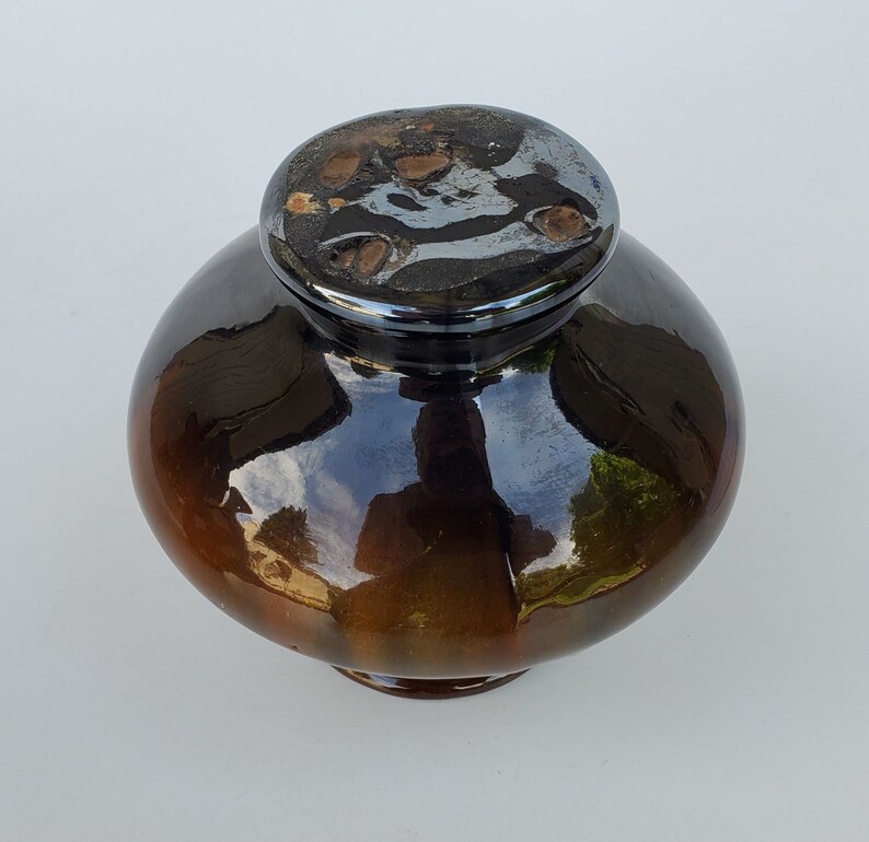 May include: A brown and black ceramic jar with a shiny glaze. The lid is black with a silver design.