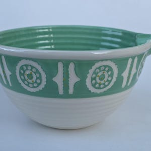 Peut inclure: Un saladier en c&eacute;ramique blanc et turquoise. Le bol a une poign&eacute;e et une bande d&eacute;corative avec des motifs circulaires et lin&eacute;aires blancs et jaunes. La moiti&eacute; inf&eacute;rieure du bol est blanche et le haut est turquoise.