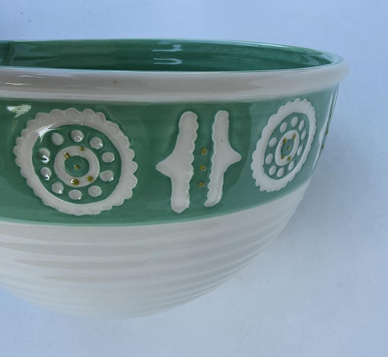 Peut inclure: Un bol en c&eacute;ramique blanc et vert. La partie sup&eacute;rieure est verte avec des motifs d&eacute;coratifs blancs. La partie inf&eacute;rieure est blanche avec des rainures horizontales. Le bol est de forme arrondie.