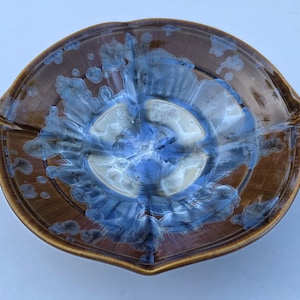 May include: A handmade ceramic serving dish with a unique design. The dish features a brown exterior with a blue and white interior. The rim has a slight upward curve, and the dish has a unique shape. The dish is approximately 10 inches in diameter.