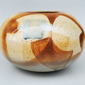 May include: A round ceramic vase with a speckled brown glaze and abstract white and brown designs.