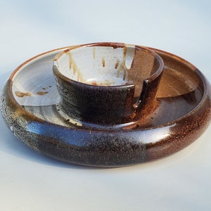 May include: A brown and white ceramic serving dish with a smaller bowl in the center. The dish has a speckled glaze and the bowl has a white glaze with brown accents.